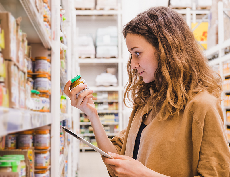 Young beautiful woman with a tablet picks baby food in a supermarket, the girl is studying the composition of the product close-up