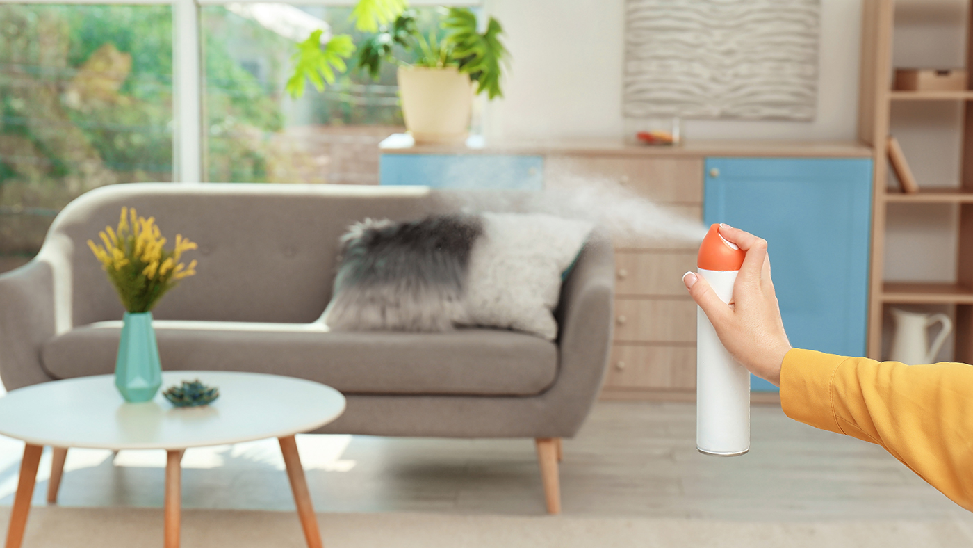 Woman spraying air freshener at home