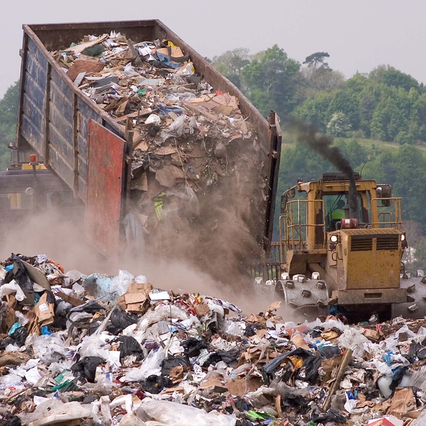 A bulldozer and garbage truck on a landfill waste site